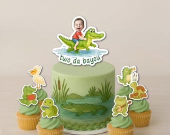 May include: A green cake and cupcakes decorated with alligator and bayou-themed toppers. The cake features a child riding an alligator and the text "two da bayou". Cupcakes have alligator, turtle, and pelican toppers.