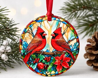 May include: A round ceramic ornament featuring a stained-glass style illustration of two bright red cardinal birds perched on a branch. The design includes green holly leaves, red berries, and a red poinsettia flower, finished with a red ribbon hanger.