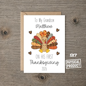 May include: A white greeting card featuring a cartoon turkey with colorful patterned feathers, four brown hearts, and black text that reads To My Grandson Matthew ON HIS FIRST Thanksgiving 2026. The card measures 5x7 inches and includes a brown envelope.