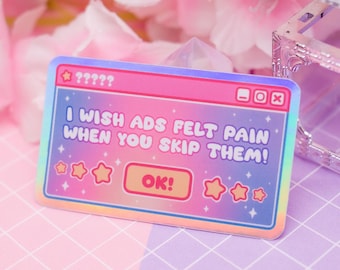 Può includere: Un adesivo olografico con un design a finestra di computer. L'adesivo ha un gradiente di rosa, blu e giallo. Il testo sull'adesivo recita "I WISH ADS FELT PAIN WHEN YOU SKIP THEM!" e "OK!" con accenti di stelle.