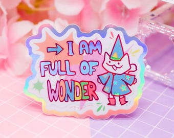 May include: A holographic sticker with the text "I AM FULL OF WONDER" and a cartoon cat wearing a wizard hat and robe. The sticker has a colorful, whimsical design with a pink, purple, and blue background.