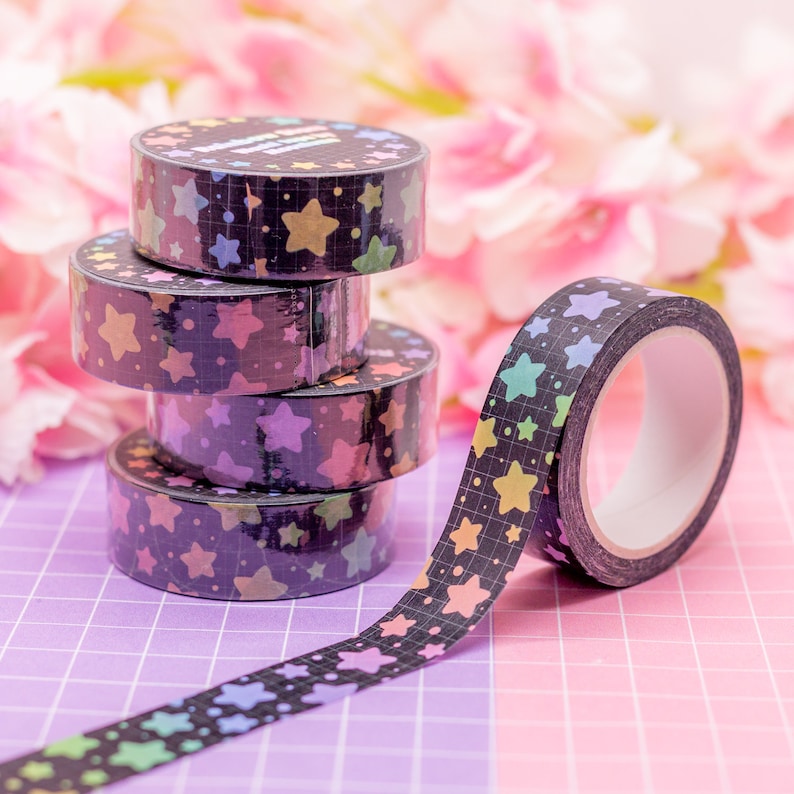 May include: A roll of black washi tape with a rainbow star pattern. The tape is unrolled and stacked on top of three other rolls of the same tape.