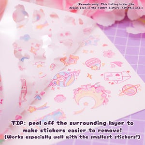 Pode incluir: Uma folha de adesivos rosa pastel e azul com uma variedade de desenhos fofos, incluindo estrelas, luas, planetas, flores e cora&ccedil;&otilde;es. Os adesivos est&atilde;o em um fundo branco e est&atilde;o parcialmente descolados para mostrar os desenhos. O texto "TIP: peel off the surrounding layer to make stickers easier to remove! (Works especially well with the smallest stickers!)" est&aacute; impresso na parte inferior da folha.