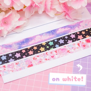 May include: Four rolls of washi tape with different designs. The top roll has a purple and blue sky with clouds and stars. The second roll has black stars on a black and white grid. The third roll has rainbow stars on a black background. The bottom roll has a pink and white design with hearts, stars, and other cute elements. The text "on white!" is visible in the lower right corner of the image.