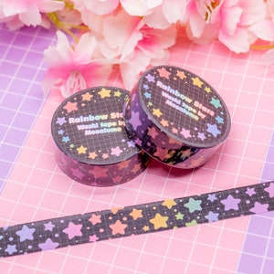 May include: Two rolls of rainbow star washi tape on a pink and purple grid background. The tape is black with rainbow stars and the text "Rainbow Stars Washi Tape by MoonLune".