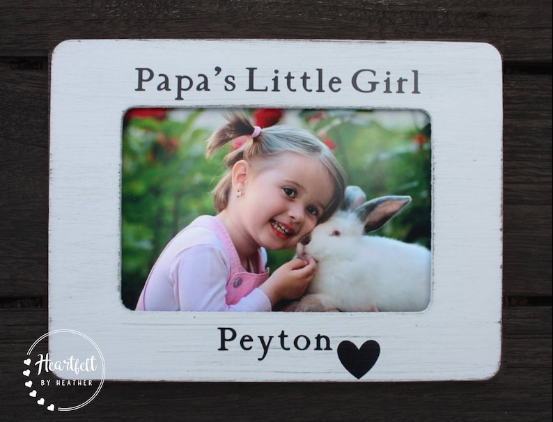 May include: White wooden picture frame with a photo of a young girl with a rabbit. The frame has the text "Papa's Little Girl" at the top and "Peyton" with a black heart at the bottom.