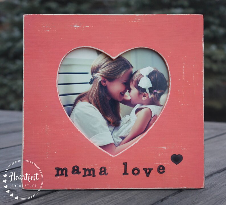 May include: A pink wooden picture frame with a heart-shaped cutout. The frame has the words "mama love" printed on the bottom. A photo of a mother and daughter is visible through the cutout.