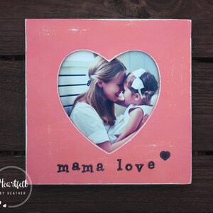 May include: Pink wooden picture frame with a heart-shaped cutout. The cutout features a photo of a mother and daughter. The text "mama love" is printed on the frame.