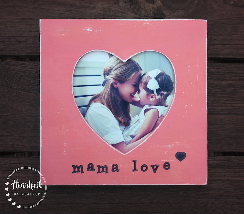May include: Pink wooden picture frame with a heart-shaped cutout. The cutout features a photo of a mother and daughter. The text "mama love" is printed on the frame.