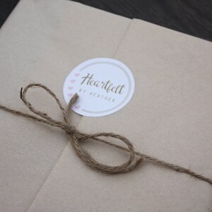 May include: A brown paper package tied with twine and a white circle sticker that says "Heartfelt by Heather" with pink hearts around the edge.