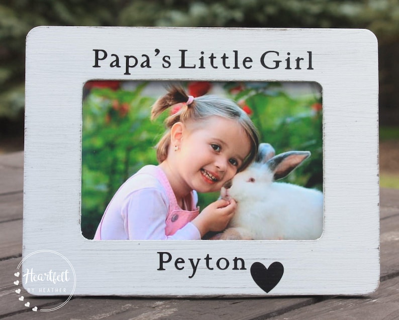 May include: White wooden picture frame with a photo of a young girl with a rabbit. The frame has the text "Papa's Little Girl" at the top and "Peyton" with a heart at the bottom.
