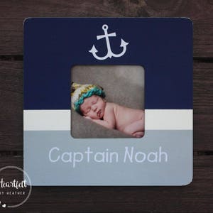 Puede incluir: Un marco de fotos de madera azul y gris con un diseño de ancla blanca y el texto "Captain Noah". El marco tiene un passe-partout blanco y una abertura transparente para una foto.