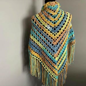 May include: A crocheted shawl with a triangular shape and fringe. The shawl is made in shades of blue, green, yellow, and orange.