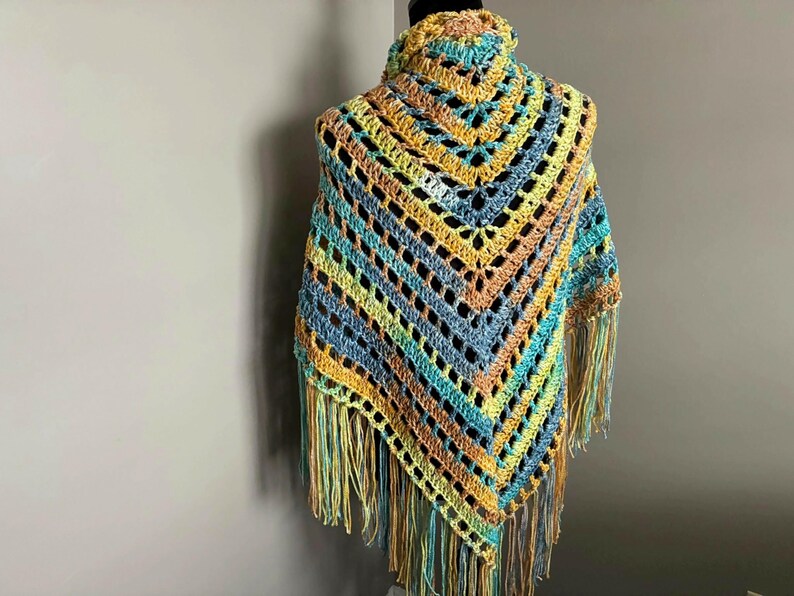 May include: A crocheted shawl with a triangular shape and fringe. The shawl is made in shades of blue, green, yellow, and orange.