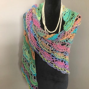 May include: A multi-coloured, handmade crochet shawl in shades of green, blue, pink, and yellow. The openwork design is draped over a black form, with a pearl necklace. The shawl's edges are scalloped.