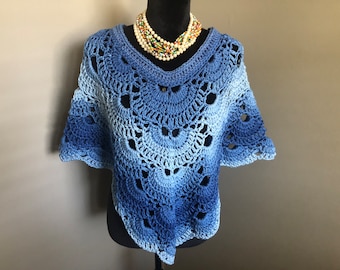 Puede incluir: Un poncho de ganchillo azul con un degradado de color de azul claro a azul oscuro. El poncho tiene un borde festoneado y un delicado diseño de calado.