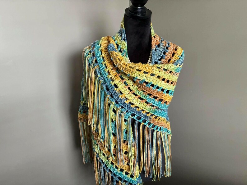 May include: A crocheted shawl with a colorful striped pattern and fringe. The shawl is made in shades of blue, green, yellow, and orange.