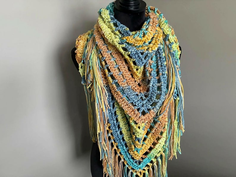 May include: A crocheted triangular shawl with a multi-colored pattern of blue, green, yellow, and orange. The shawl has long fringe around the edges.