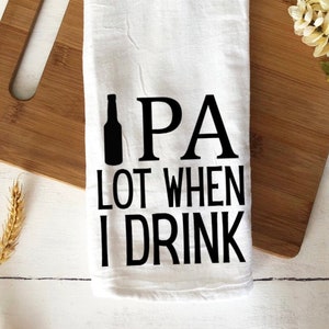 May include: White kitchen towel with black text that reads "IPA lot when I drink". A black silhouette of a beer bottle is to the left of the text.