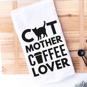 May include: White kitchen towel with black text that reads "Cat Mother Coffee Lover" with a black silhouette of a cat and a coffee cup.