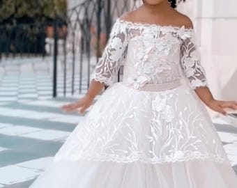 May include: An off-the-shoulder white dress featuring three-quarter length lace sleeves, a bodice adorned with floral lace appliques, a defined waistline, and a voluminous tulle skirt. The text MySweetQueenUS is printed at the bottom of the image.