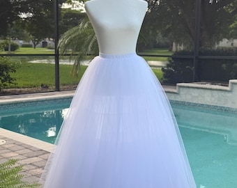 May include: A white tulle skirt displayed on a mannequin. The skirt features a high-waisted design with a full, voluminous silhouette created by multiple layers of sheer, fine netting fabric that extend from the waist down to the hemline.