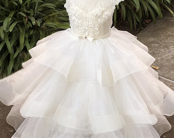 Puede incluir: Vestido de tul blanco con un corpiño de cuentas y una faja de satén. El vestido tiene varias capas de tul y un dobladillo festoneado.