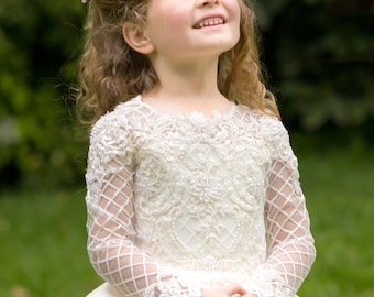 May include: A cream-coloured long-sleeve dress featuring an intricate bodice with beadwork and embroidery, a lattice-patterned mesh overlay on the sleeves, and a full skirt. A large pink flower accessory is pinned to the hair on the side.
