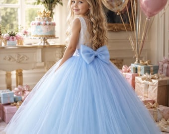 May include: A floor-length dress featuring a white sleeveless bodice and a voluminous light blue tulle skirt. The waist is accented with a large, matching light blue bow at the back. The skirt has multiple layers of sheer fabric creating a full silhouette.