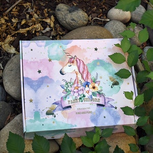 Pu&ograve; includere: Una scatola rosa e blu con un design ad acquerello di un unicorno con criniera e coda rosa. L'unicorno &egrave; circondato da fiori e stelle. La scatola ha il testo "Fairy Unicorn" e "Noble Qualities Kind and Pure".