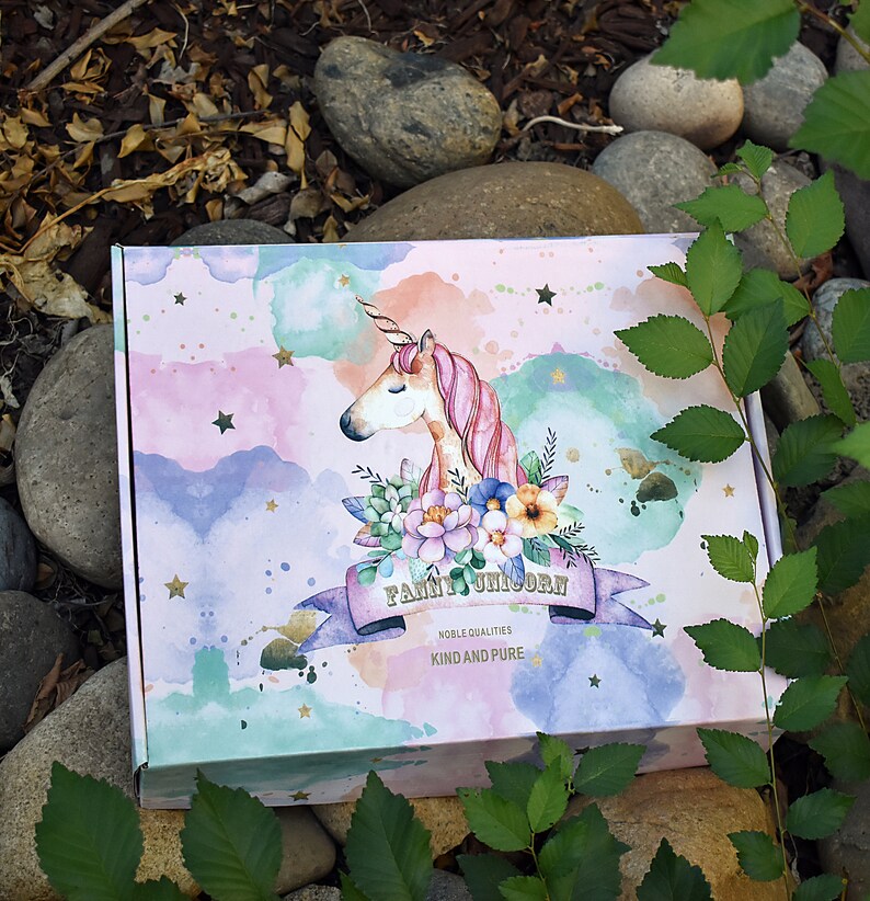 Pu&ograve; includere: Una scatola rosa e blu con un design ad acquerello di un unicorno con criniera e coda rosa. L'unicorno &egrave; circondato da fiori e stelle. La scatola ha il testo "Fairy Unicorn" e "Noble Qualities Kind and Pure".
