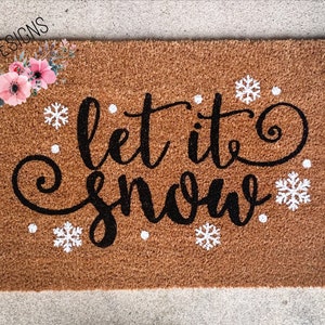 Puede incluir: Una alfombra de coco marr&oacute;n con el texto "Let it snow" en letras cursivas negras. Copos de nieve blancos y puntos est&aacute;n dispersos alrededor del texto.