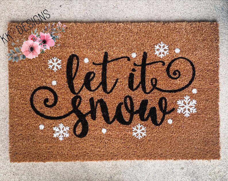 Puede incluir: Una alfombra de coco marr&oacute;n con el texto "Let it snow" en letras cursivas negras. Copos de nieve blancos y puntos est&aacute;n dispersos alrededor del texto.