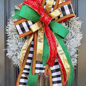 May include: A festive Christmas wreath with a silver base and a large bow. The bow features red, green, gold, and black and white checkered ribbons. Some ribbons have musical notes printed on them.