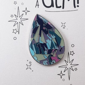 May include: A white card with black text that reads "You're such a GEM!" with a black and white star design. A blue, green, and pink enamel pin shaped like a teardrop is on the card.