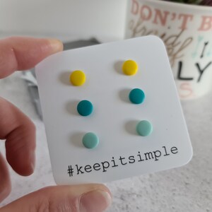 May include: A set of six colorful stud earrings on a white card with the text "#keepitsimple". The earrings are yellow, teal, and light blue.