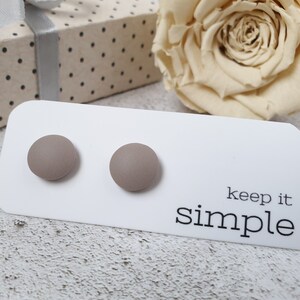 May include: A pair of small, round, light brown stud earrings on a white card with the text "keep it simple".