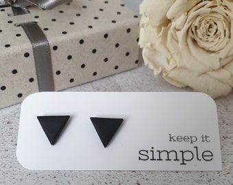 Puede incluir: Pendientes de botón triangulares negros sobre una tarjeta blanca con el texto "keep it simple". Los pendientes tienen un acabado mate. Una caja de regalo con lazo y una rosa crema están en el fondo.