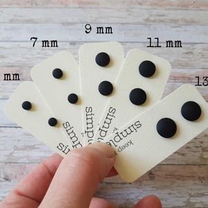 May include: Six cards with black round studs of different sizes, labeled with their diameter in millimeters: 5 mm, 7 mm, 9 mm, 11 mm, and 13 mm. The cards are arranged in a fan shape, with the largest stud on the right and the smallest on the left. The cards have the text "keep it simple" printed on them.