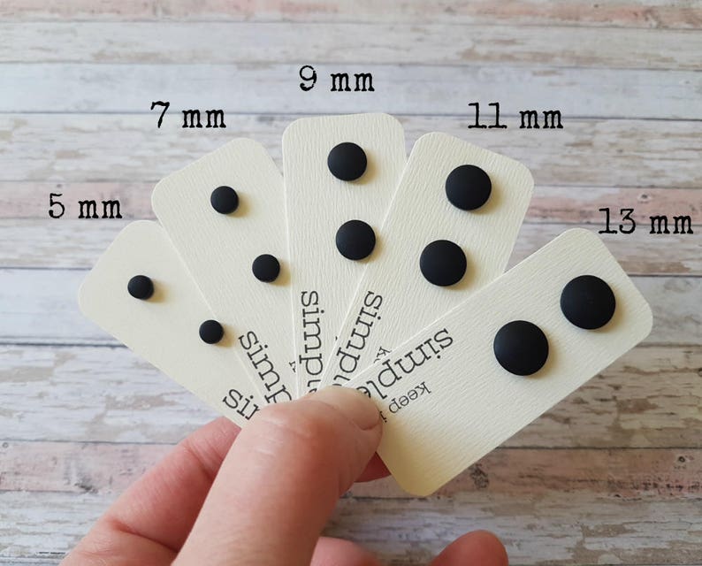 May include: Six cards with black round studs of different sizes, labeled with their diameter in millimeters: 5 mm, 7 mm, 9 mm, 11 mm, and 13 mm. The cards are arranged in a fan shape, with the largest stud on the right and the smallest on the left. The cards have the text "keep it simple" printed on them.