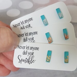 May include: Turquoise rectangular stud earrings with silver, copper, and gold metallic detailing. The earrings are presented on white cards with the text "Never let anyone dull your Sparkle."