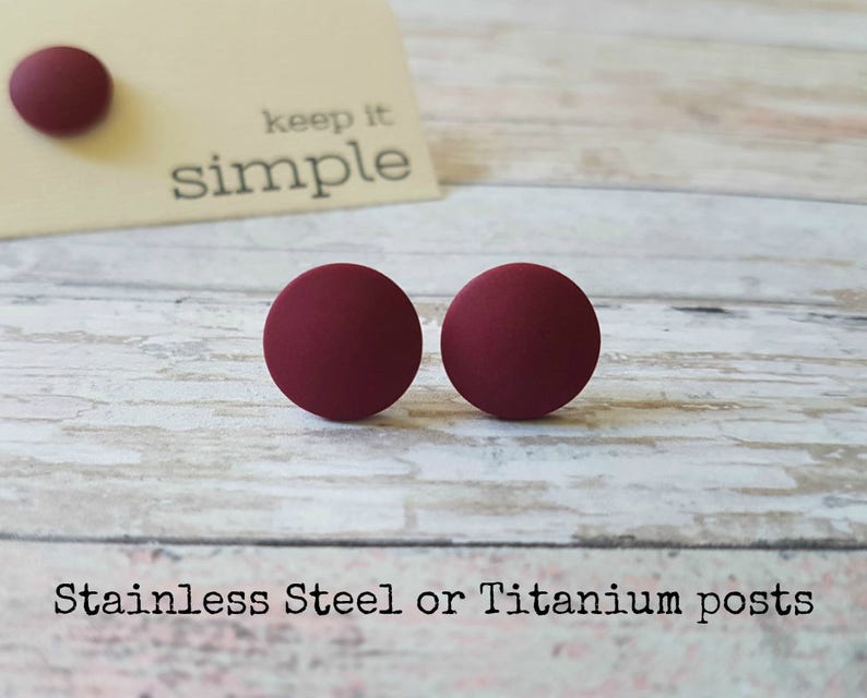 May include: A pair of burgundy stud earrings with stainless steel or titanium posts. The earrings are round and have a matte finish. The text "keep it simple" is visible in the background.