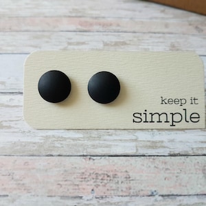 May include: Two black round stud earrings on a white card with the text "keep it simple".