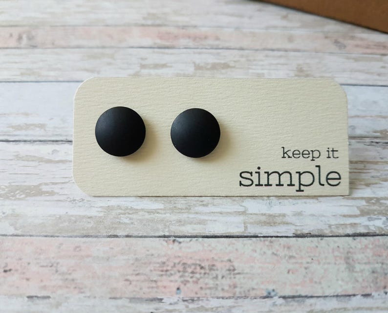 May include: Two black round stud earrings on a white card with the text "keep it simple".