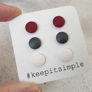 Op de afbeelding: Een set van vier paar ronde oorstekers in bordeauxrood, donkergrijs en wit, gepresenteerd op een witte kaart. De kaart heeft de tekst "#keepitsimple". De oorbellen zijn klein en minimalistisch.