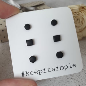 Könnte beinhalten: Ein Set mit sechs schwarzen Ohrsteckern in drei verschiedenen Formen: Kreis, Quadrat und Sechseck. Die Ohrstecker sind auf einer weißen Karte mit dem Text "#keepitsimple" abgebildet.