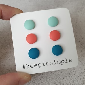 Può includere: Un set di sei orecchini a bottone rotondi in turchese, verde menta e corallo. Gli orecchini sono esposti su una carta bianca con il testo "#keepitsimple".