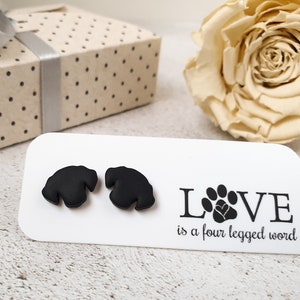 Può includere: Un paio di orecchini a bottone a forma di impronta di zampa nera su una carta bianca con il testo "LOVE is a four legged word".