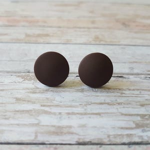 K&ouml;nnte beinhalten: Ein Paar braune runde Ohrstecker. Die Ohrringe sind aus einem glatten, matten Material.