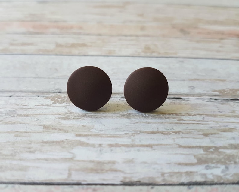 K&ouml;nnte beinhalten: Ein Paar braune runde Ohrstecker. Die Ohrringe sind aus einem glatten, matten Material.